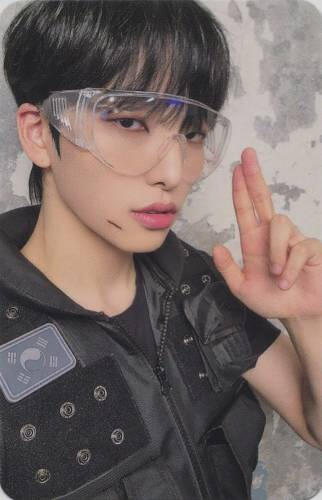 Seoho wearing a black tactical vest, clear goggles, and making a finger gun