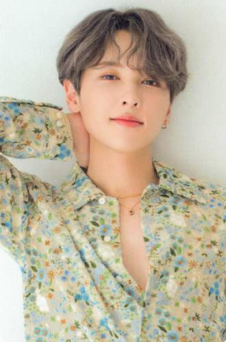 Photocard of Rie wearing an open floral button up and holding the back of his neck, lightly smiling