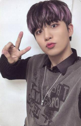 Jongho wearing a grey sweater vest and black sweater and making a peace sign