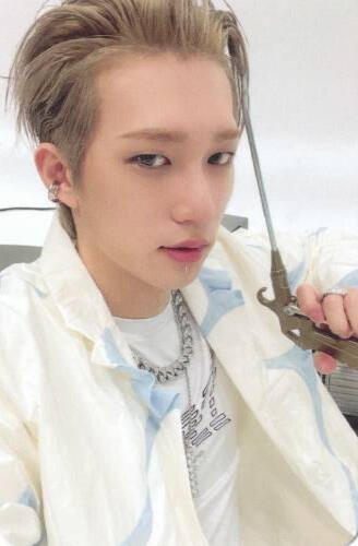 Photocard of Theo wearing an open white shirt over a white tshirt, holding a toy gun by his face