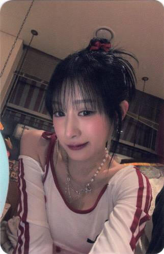 Photocard of Chaei taking a selfie with her arm fully extended, half smiling
