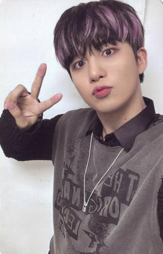 Jongho wearing a grey sweater vest and black sweater and making a peace sign