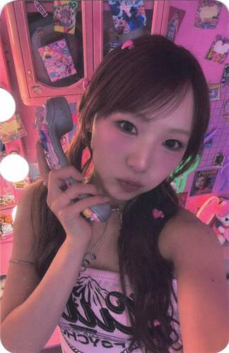 Photocard of Yume holding a phone to hear ear in a pink room