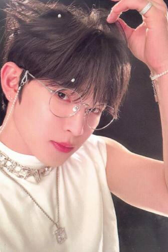 Photocard of Leedo wearing a white sleeveless shirt, silver jewelry, and thin silver glasses with a glasses chain, holding a piece of his hair