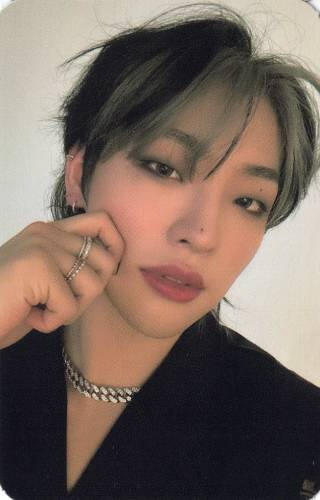 Photocard of Mujin wearing a black coat and pinching his cheek