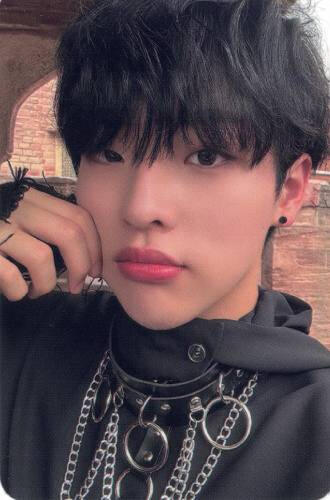 Photocard of Mujin wearing a black outfit with a black, chained choker, and pinching his cheek
