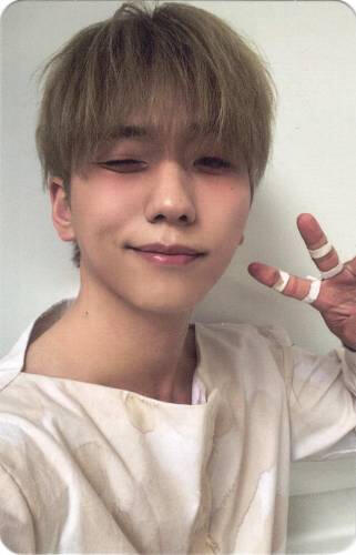 Photocard of Gunil smiling, winking, and making a peace sign with bandaged fingers