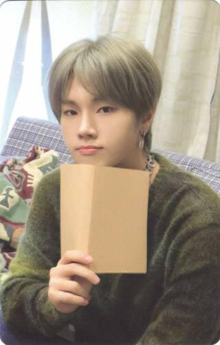 Photocard of Jungsu holding a paper up to his face and looking over it