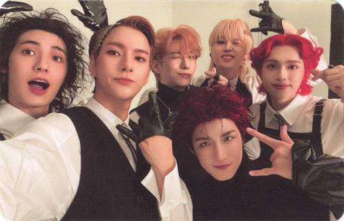 A group photocard of Xdinary Heroes smiling and making "rock on" hand signs