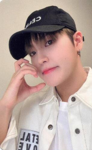 Photocard of Louis wearing a white jacket and black baseball cap making a half-heart with an animal ear with his hand against his cheek