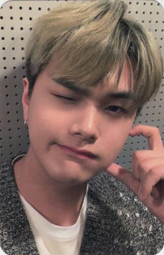 Photocard of Jahan in a loose knit grey sweater, making a cheek heart and winking