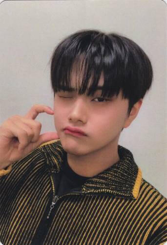 Photocard of Jahan wearing a yellow and black sweater, making a heart against his cheek, and winking