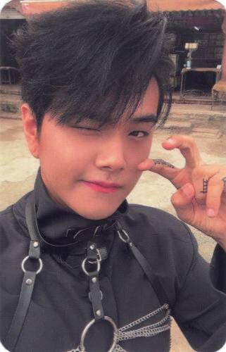 Photocard of Jahan wearing a black outfit with a black harness, holding a peace sign up and winking