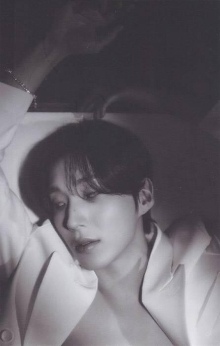 Photocard of Moon Jongup wearing an open white suit jacket with nothing under, holding his arms loosely above him