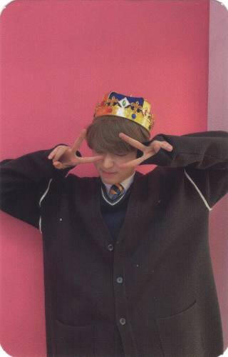 Photocard of Arthur wearing a crown and black blazer and making peace signs over his eyes