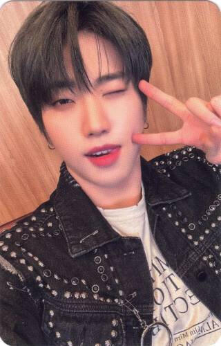 Photocard of Dann wearing a studded black jacket, making a peace sign, and winking