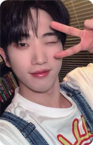 Photocard of Dann winking and making a peace sign while wearing a sweater with denim overalls