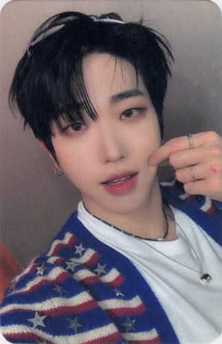 Photocard of Dann wearing a blue, white, and red sweater and pinching his cheek