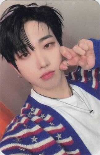 Photocard of Dann wearing a red white and blue sweater and making a curled peace sign
