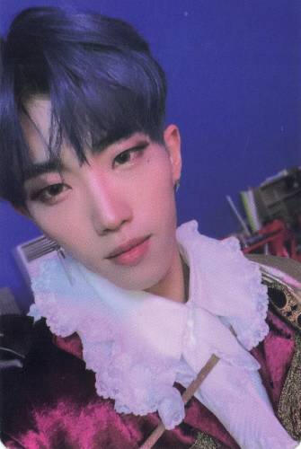 Photocard of Dann wearing a red velvet outfit and a fluffy cravat, looking into the camera