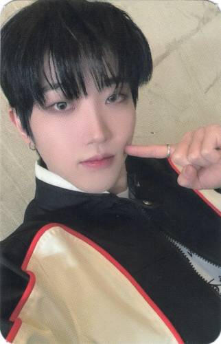 Photocard of Dann wearing a black, white, and red racing jacket and poking his cheek