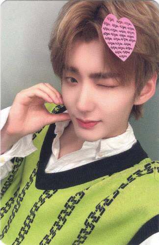 Photocard of Hwon making a cheek heart with a pink heart-shaped sticky note on his hair