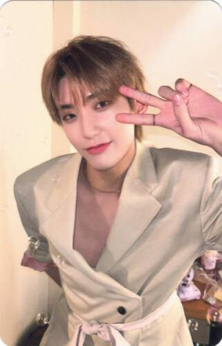 Photocard of Hwon wearing a tan suit jacket and leaning forward while making a peace sign