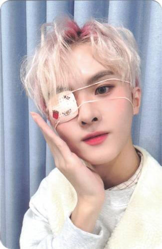 Photocard of Ivan holding his cheek while wearing an eyepatch