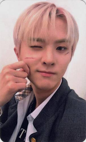 Photocard of Ivan pinching his cheek and winking with two cuts on his face