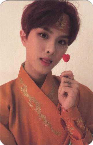 Photocard of Ivan in orange hanbok holding a red heart-shaped lollipop