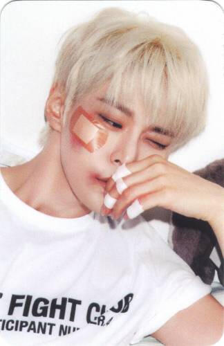 Photocard of Doyoung with a large bandaid on his cheek, looking off to the side with a hand in front of his face