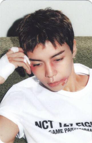 Photocard of Johnny with cuts on his face, resting his head on his hand and looking down