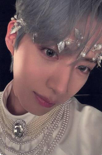 A photocard of Xion with grey hair, a silver leaf headband, and a shiny white shirt with his face close to the camera